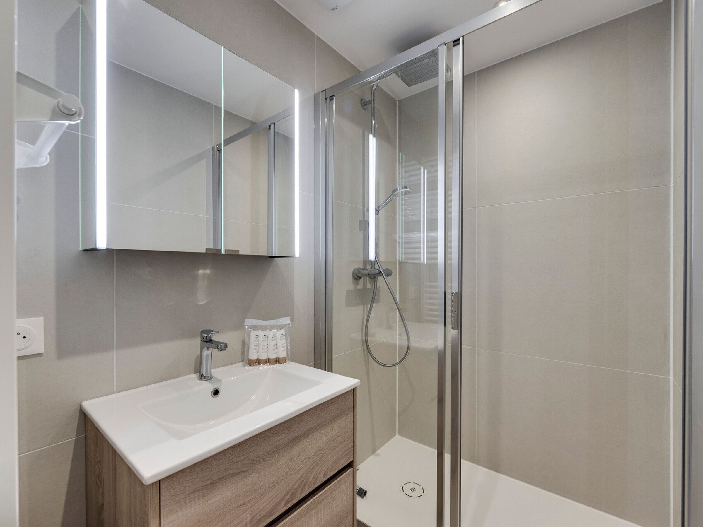 A modern bathroom with a glass shower enclosure, a white sink with a wooden vanity, and a large mirror above the vanity.