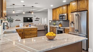 A modern kitchen with wooden cabinets, a stainless steel refrigerator, and a marble island with a bowl of lemons. - Dobson Ranch, Farmhouse Casual, Pool & Games! (Mesa)