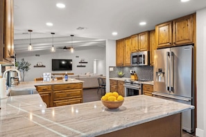 A modern kitchen with wooden cabinets, a stainless steel refrigerator, and a marble island with a bowl of lemons.