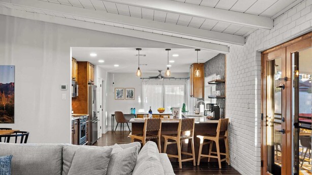 A modern kitchen with white brick walls, wooden cabinets, and a dining area with a table and chairs. - Dobson Ranch, Farmhouse Casual, Pool & Games! (Mesa)