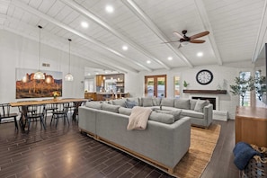 A spacious living area with a large sectional sofa, dining table, and chairs, a kitchen in the background, and a fireplace.