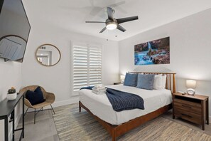 A bedroom with a bed, bedside tables, a ceiling fan, a wall-mounted TV, a mirror, and a painting.