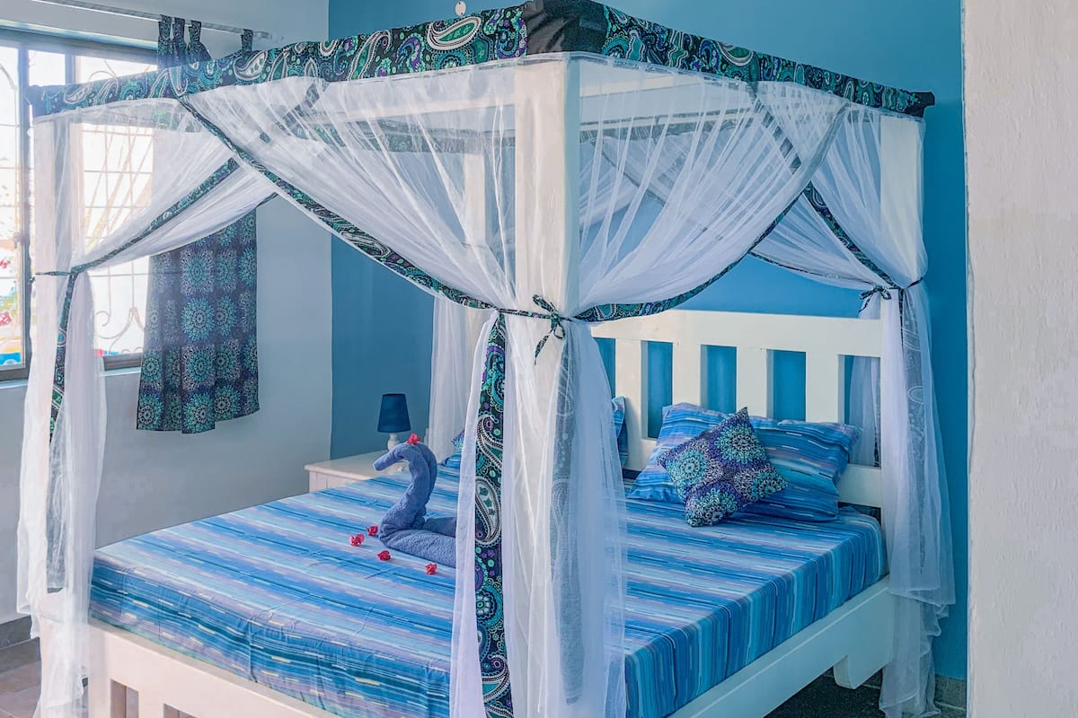 Un lit à baldaquin, un ventilateur de plafond et une fenêtre avec des rideaux.