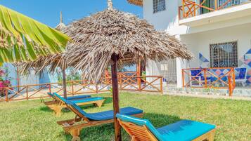 Un hotel con tejado de paja, sillones de madera y un balcón con baldosas.