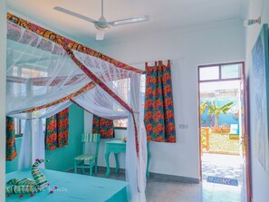 A room with a bed under a canopy, a desk, a chair, and a window with curtains. - PINEAPPLE HOUSE (Nungwi)