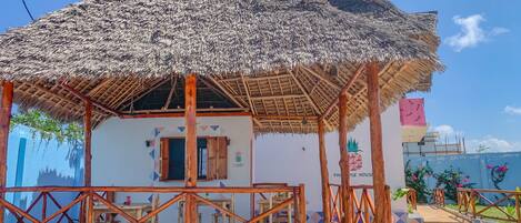 A thatched-roof structure with a wooden railing and a tiled floor, likely a guest area or outdoor seating.