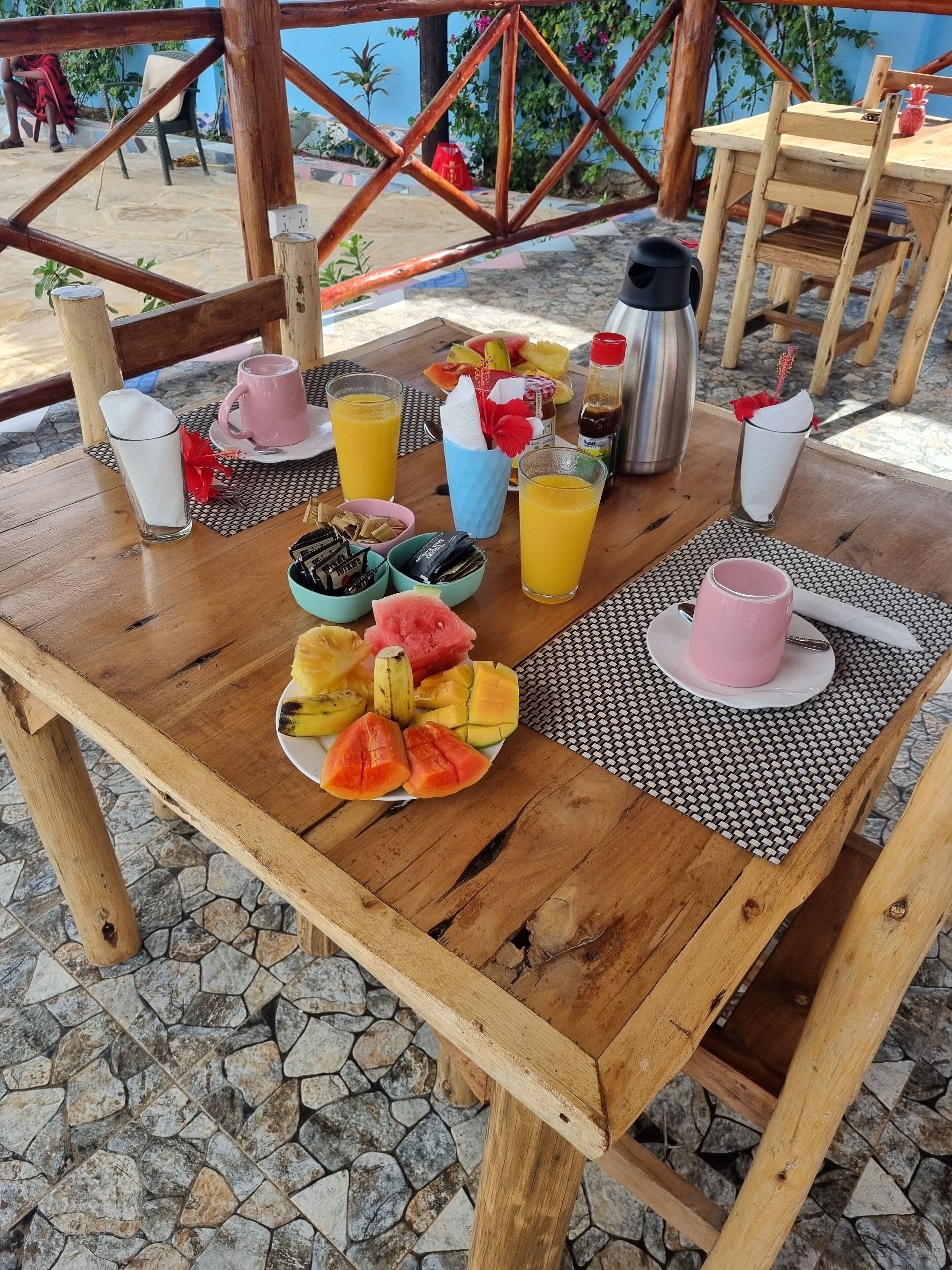 A wooden table with a fruit platter, drinks, and a thermos.