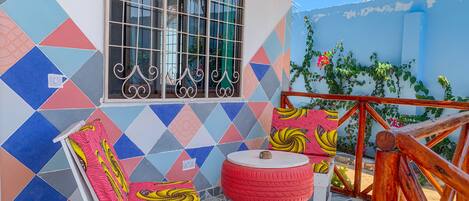 Una habitación con suelo de baldosas, una ventana con rejas de metal, una pared colorida, una mesa redonda pequeña y un banco de madera.