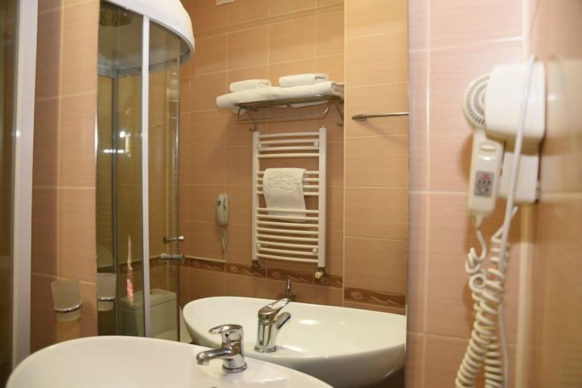 Un baño con cabina de ducha de vidrio, un lavamanos con espejo, un perchero con toallas y un secador de pelo en la pared.