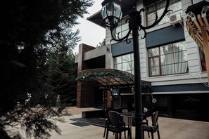 An outdoor seating area with a table and chairs, a decorative umbrella, and a building with large windows and a brick facade. - Hotel Florence (Chisinau)