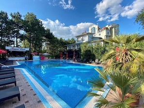 Piscina com espreguiçadeiras, um Royal Cafe e um edifício grande com uma cúpula ao fundo.