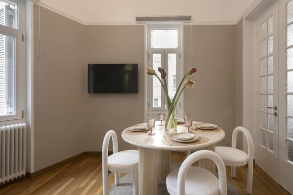 Una sala da pranzo con un tavolo rotondo, quattro sedie, un vaso con fiori e un televisore a schermo piatto appeso al muro.