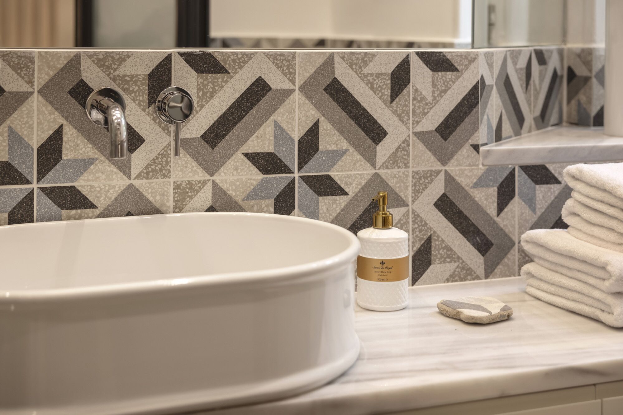 A bathroom with a large oval sink, a faucet, a bottle of lotion, and a stack of towels.