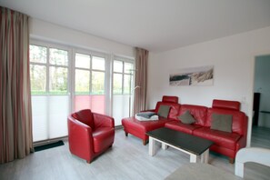 A modern living room with a red leather sofa set, a small coffee table, and a large window with curtains. - Ferienwohnung mit 3- Zimmern auf ca. 70m² im EG mit Terrasse im Haus Paul (Wyk auf Föhr)