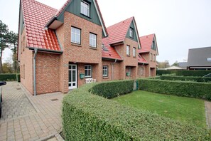 A multi-story brick building with red-tiled roofs, a paved driveway, and well-maintained hedges. - Ferienwohnung mit 3- Zimmern auf ca. 70m² im EG mit Terrasse im Haus Paul (Wyk auf Föhr)