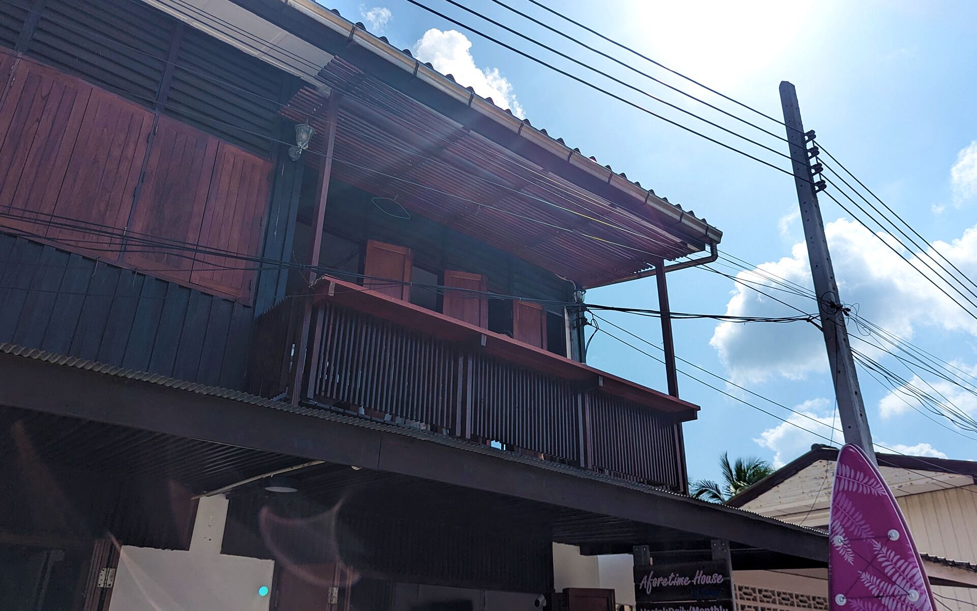 Un edificio de dos pisos con un balcón, un letrero que dice 'Aforetime House' y un poste de electricidad con cables.