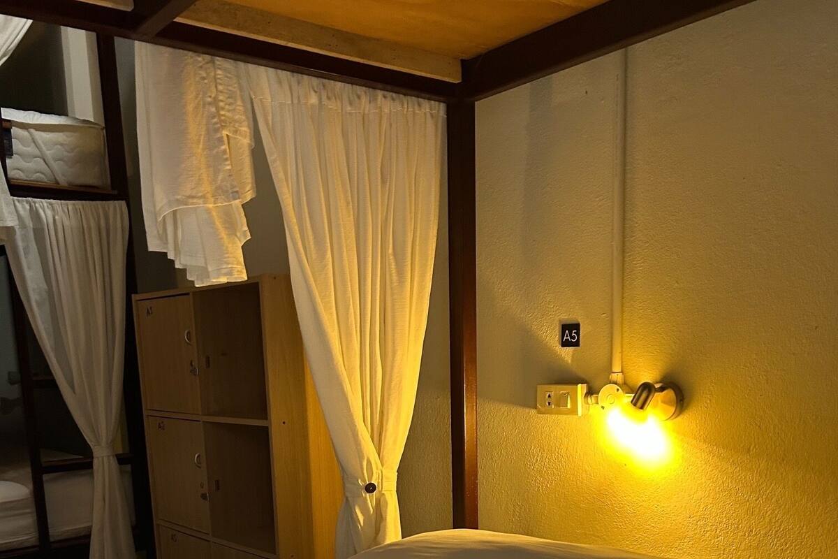 A bed with white linens, a wooden wardrobe, and a wall-mounted light fixture.