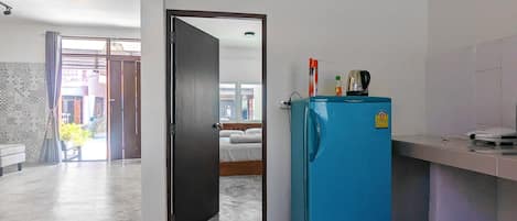 A room with a blue refrigerator, a bed, and a bathroom visible through an open door.