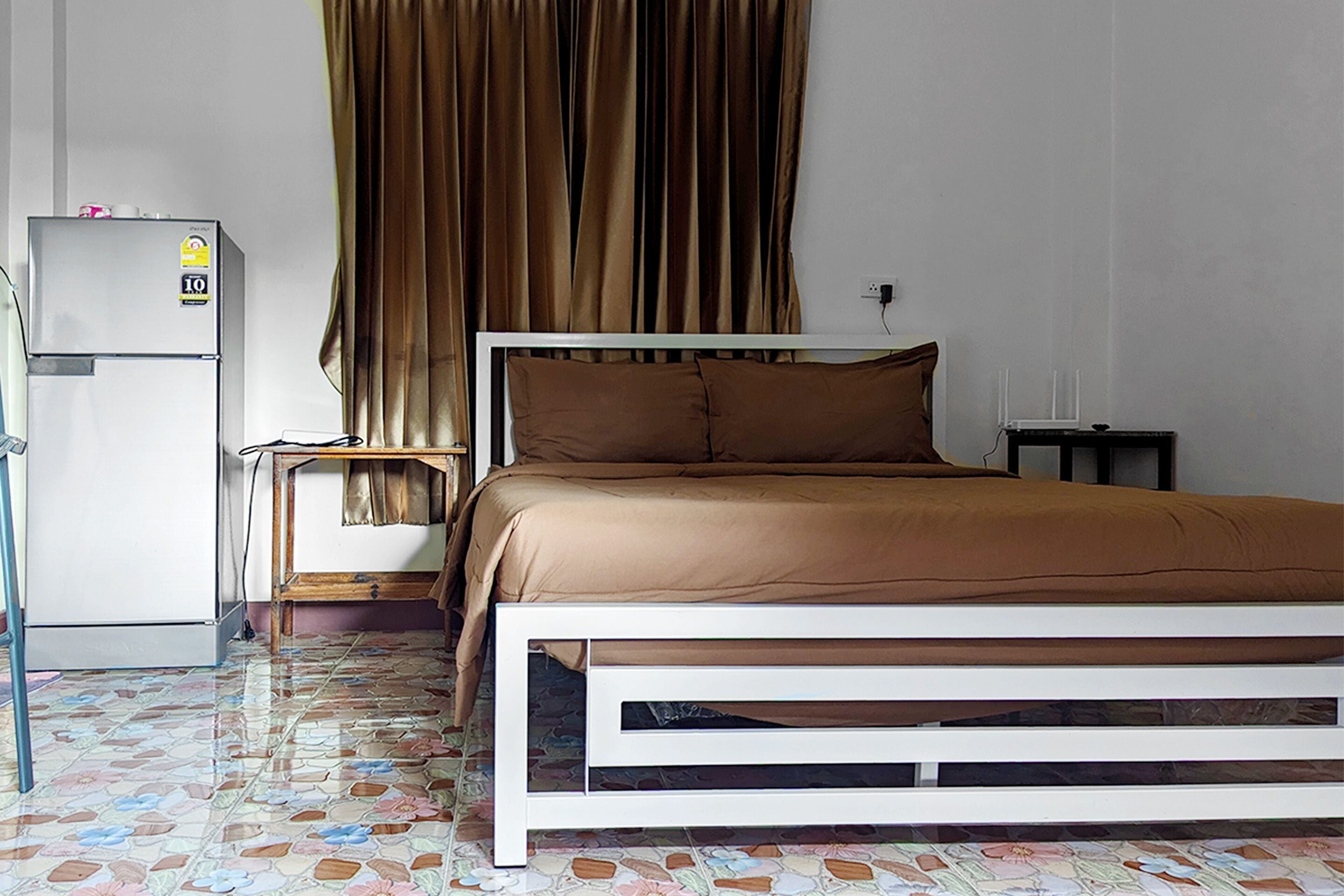 Un dormitorio con cama, mesita de noche, refrigerador y cortinas.