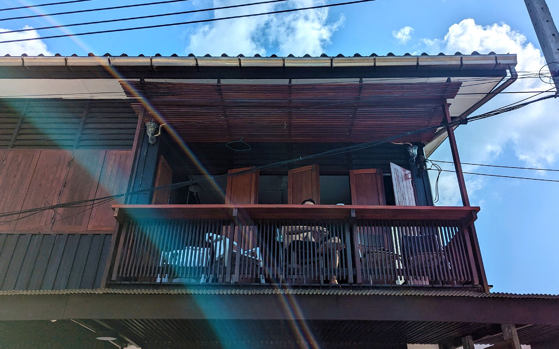 Un balcone in legno con tettoia metallica, circondato da linee elettriche.