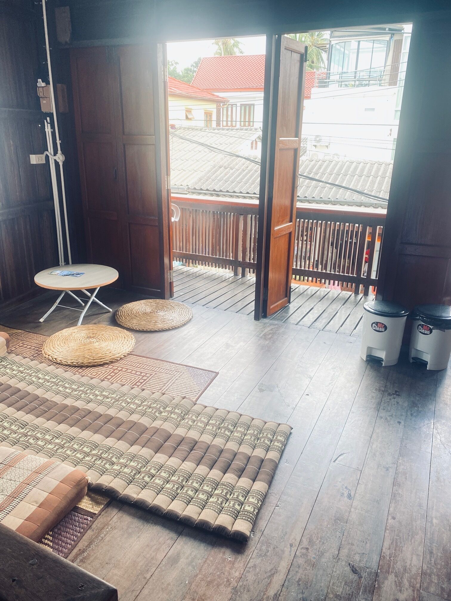 A room with a wooden floor, a small round table, a woven mat, and a sofa with patterned cushions.