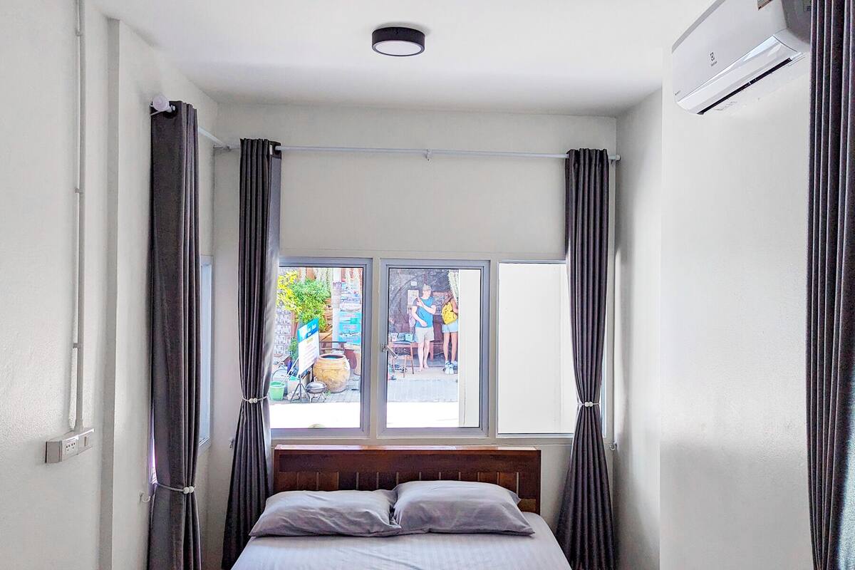 A bedroom with a bed, a window, curtains, and an air conditioning unit.