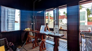 A room with a large window, a wooden table, and a view of a residential area. - MAI Place by Aforetime (Koh Samui)