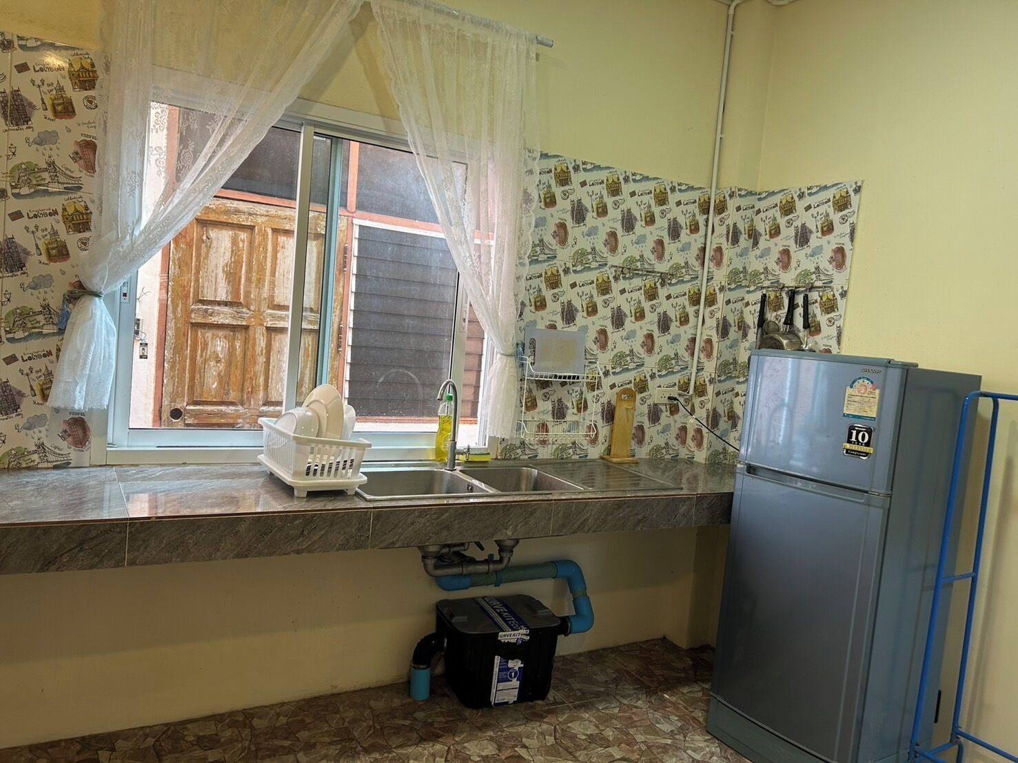 A small kitchen with a window, a sink, a refrigerator, and a water dispenser.