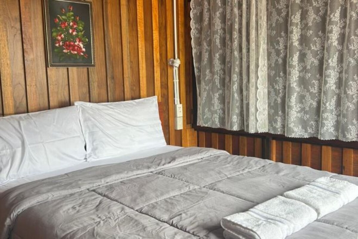 A bed with a grey quilt, white pillows, and a wooden headboard.