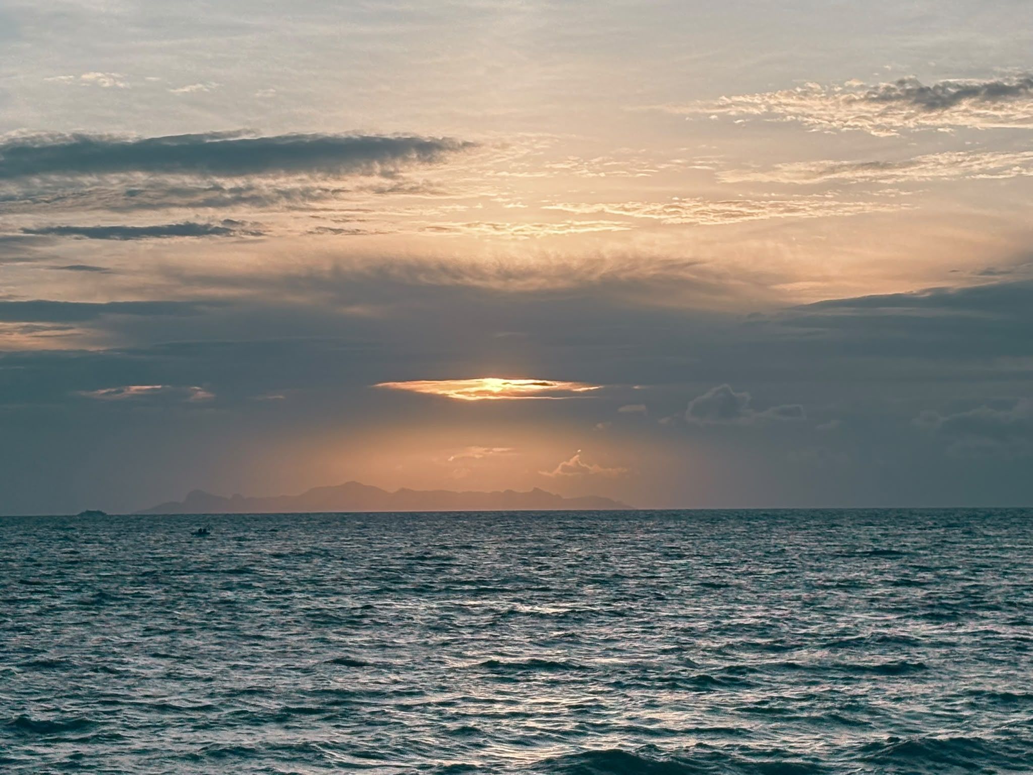 Un cuerpo de agua con una línea de horizonte y un sol parcialmente oculto por nubes.