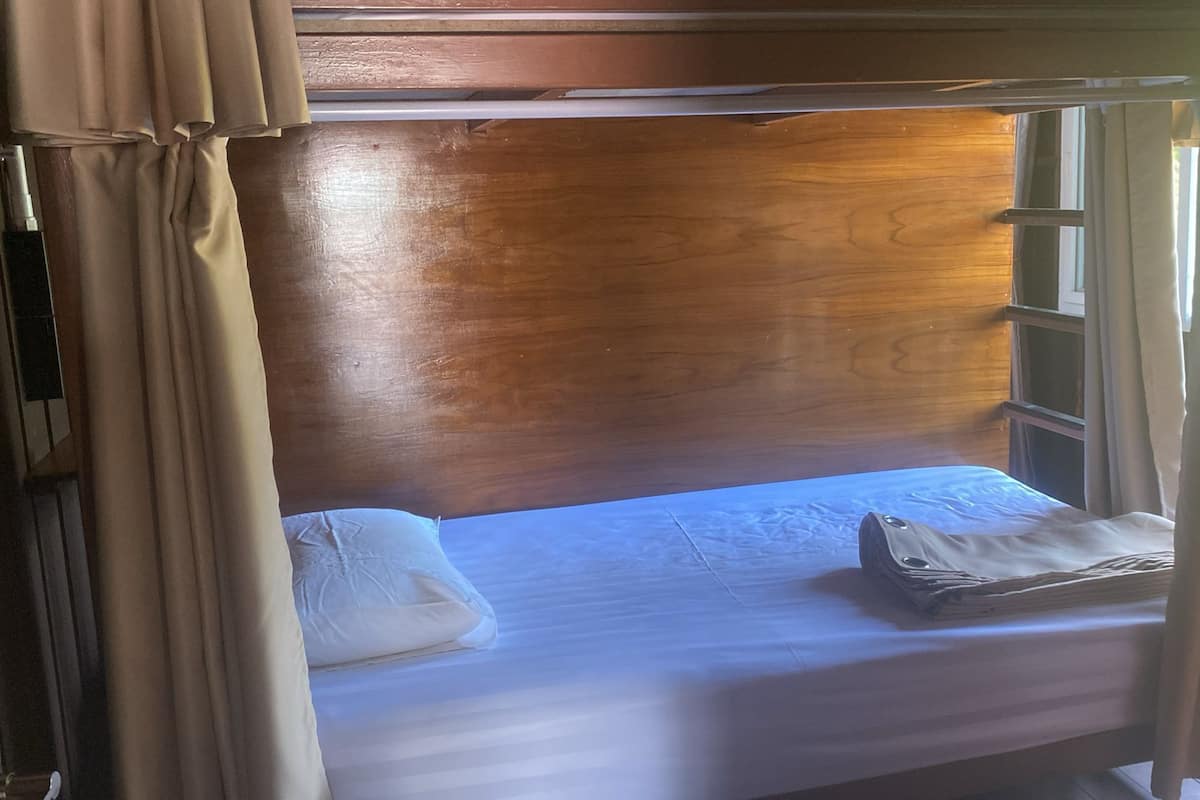 A single bed with a wooden headboard, a window with curtains, and a white pillow on the bed.