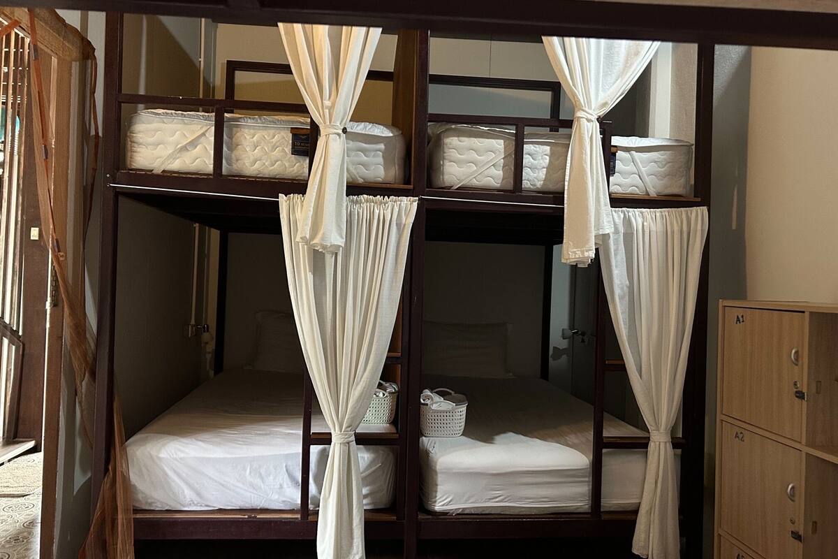 A bunk bed room with white bedding and curtains, wooden furniture, and a small basket on the lower bunk.