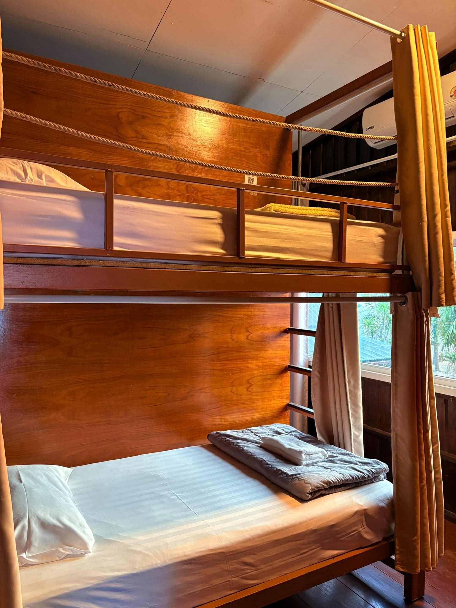 A bunk bed with a wooden headboard, a lower bunk with a pillow and blanket, and a window with curtains.