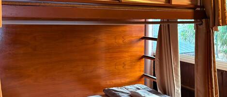 A bunk bed with a wooden headboard, a lower bunk with a pillow and blanket, and a window with curtains.