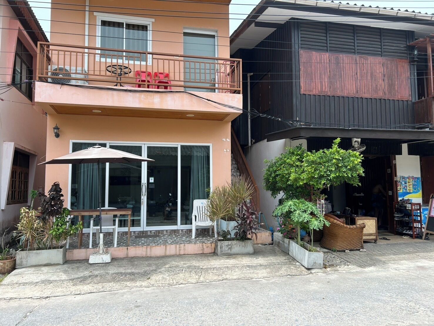 A two-story building with a balcony, outdoor seating, and potted plants.