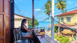 A person seated at a wooden table with a view of the sea and palm trees. - MAI Place by Aforetime (Koh Samui)