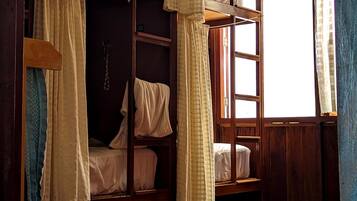 A room with two wooden bunk beds, a window with curtains, and a wall-mounted chain.