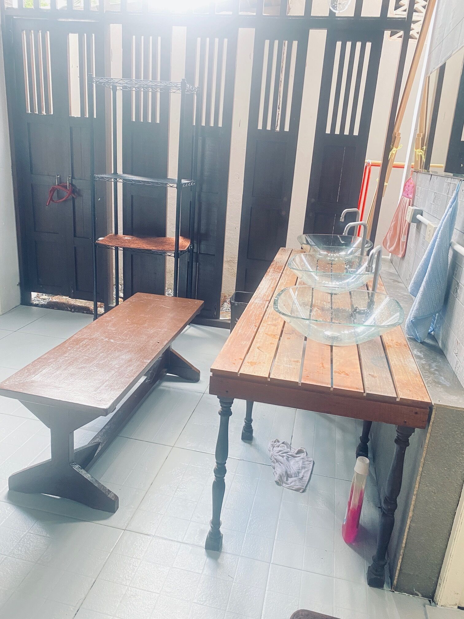 A room with a wooden table, a metal bench, and a glass-top table. There is a door with a metal gate in the background.