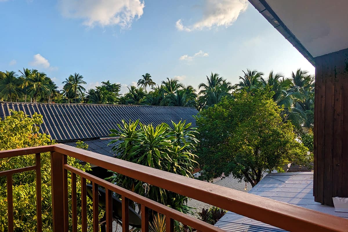 A balcony with a view of a traditional tiled roof, lush greenery, and palm trees.