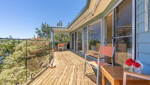 Een houten terras met tuinmeubilair, een glazen balustrade en uitzicht op een tuin.