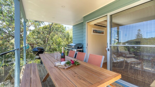 A wooden table with two glasses and a bottle, a grill, and a sliding glass door to a patio with outdoor furniture.