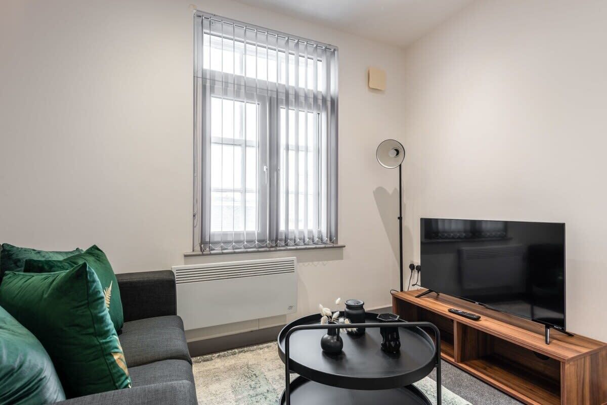 A modern living room with a grey sofa, a black coffee table, a flat-screen TV, and a window with blinds.