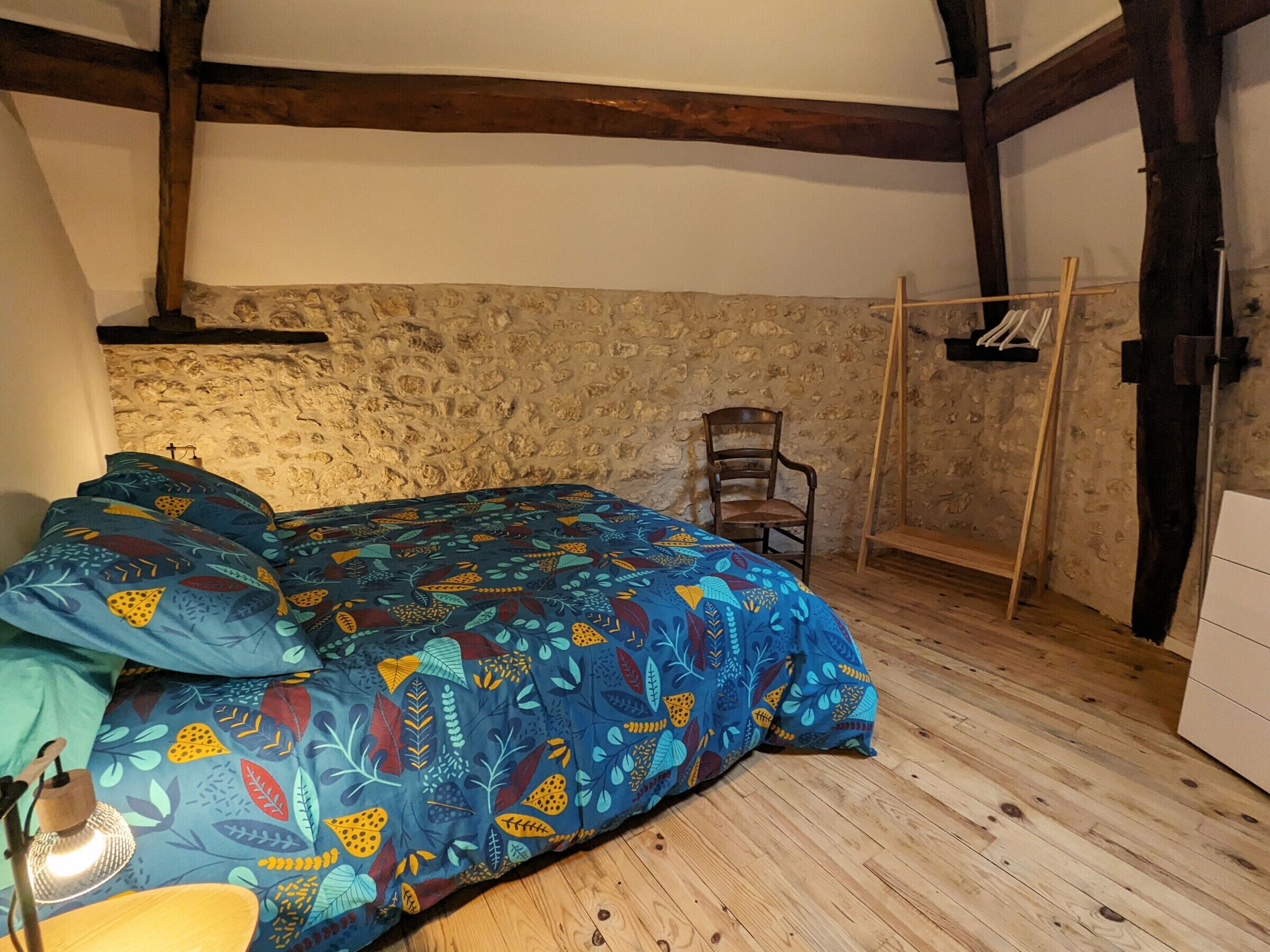 A bedroom with a bed, a chair, a wooden floor, and a stone wall.