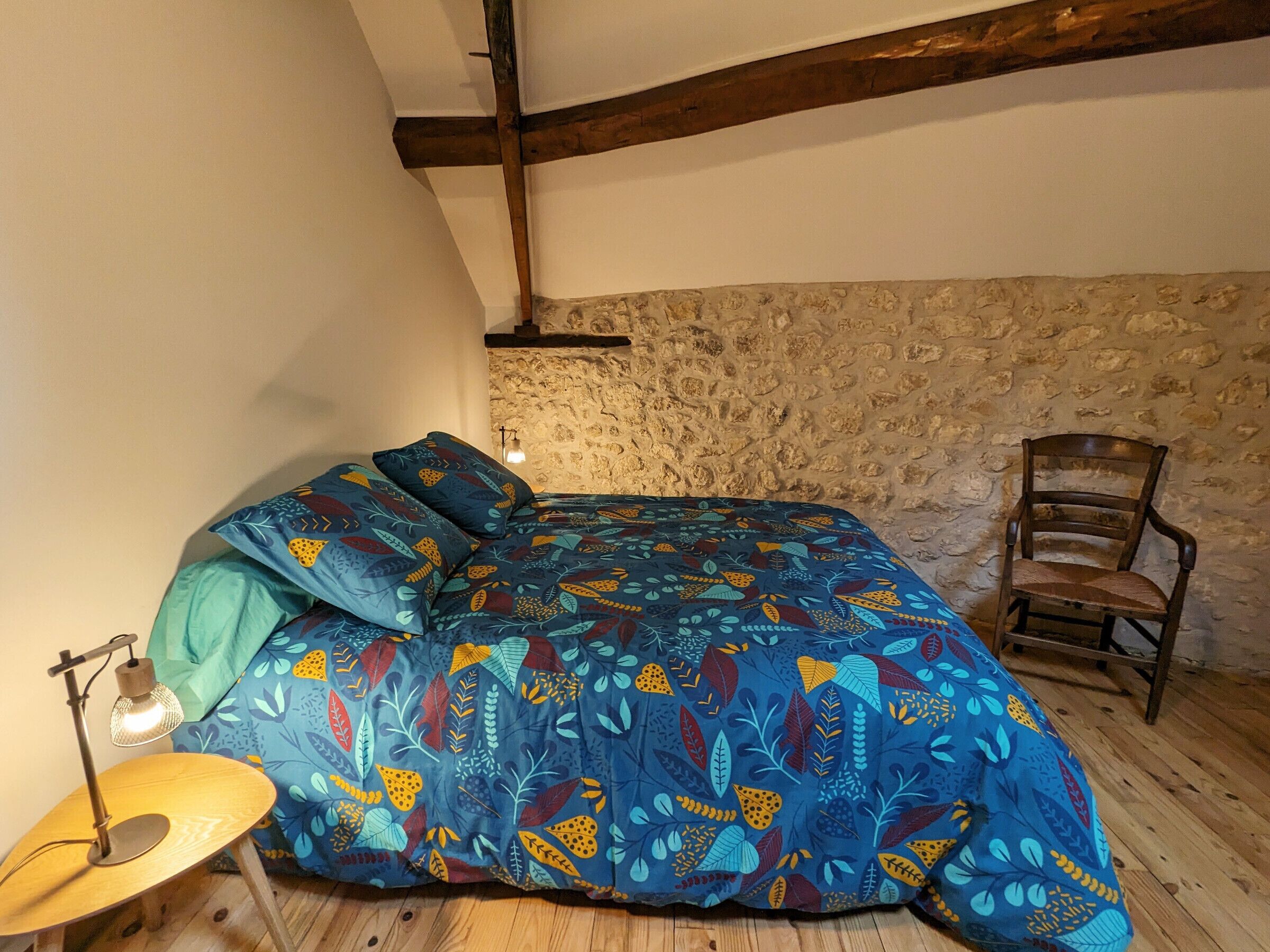 Une chambre à coucher avec un lit, une chaise, une lampe et un mur en pierre.