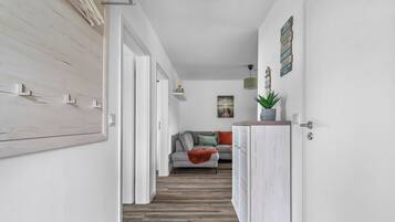Ein Flur mit Holzboden, einem grauen Sofa mit Kissen, einer roten Decke und einem weißen Schrank mit Pflanze.