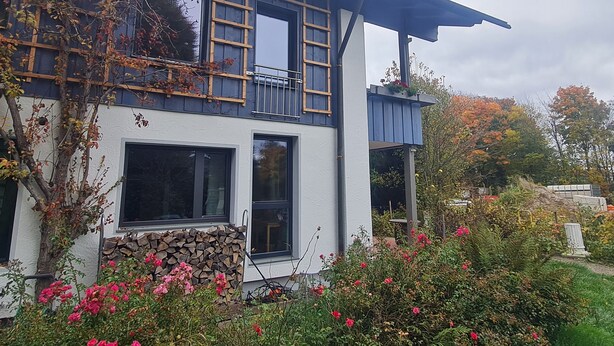 Een modern huis met twee verdiepingen, een balkon, grote ramen en een stenen muur.