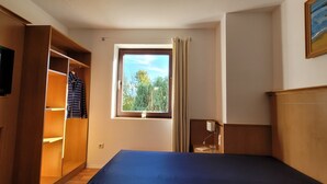 Een hotelkamer met een bed, een aan de muur bevestigde televisie, een kledingkast en een raam met uitzicht op bomen.