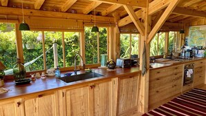 Une cuisine en bois dotée d’une grande fenêtre, d’un évier, d’une cuisinière et d’un plan de travail sur lequel sont disposés divers objets.