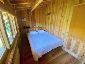 A wooden cabin room with a bed, a window, and a radiator.