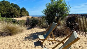 Deux chaises de plage sont placées sur une portion de sable, avec une clôture en bois et de la végétation en arrière-plan.